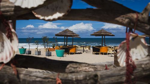 Thatched roofs and chairs at beach against sky