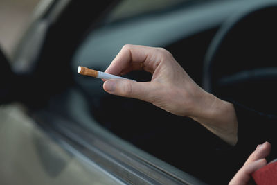 Cropped hand holding cigarette while sitting in car