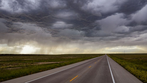 Empty country road against cloudy sky