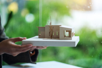 Cropped hand of woman holding model house on table