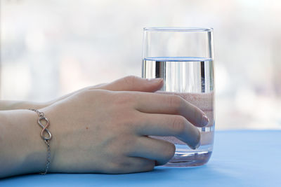 Cropped hand of woman holding water glass on table