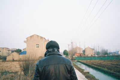 Rear view of man standing on field against buildings