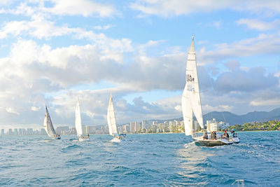 Sailboats sailing in sea against cloudy sky