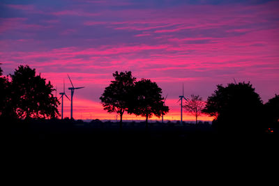 Silhouette trees on landscape against orange sky