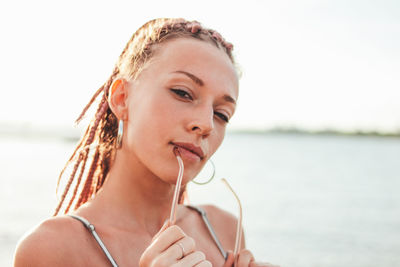 Close-up portrait of young woman holding sunglasses against lake