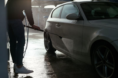 Cropped unrecognizable man with hose washing car at washing station