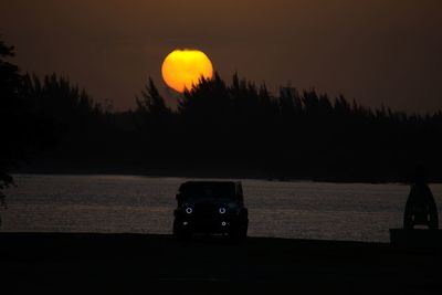 Silhouette vehicle on land against sky during sunset