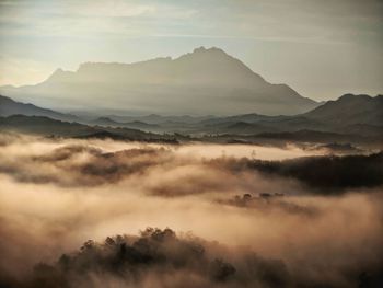 Scenic view of mountains in foggy weather during sunset