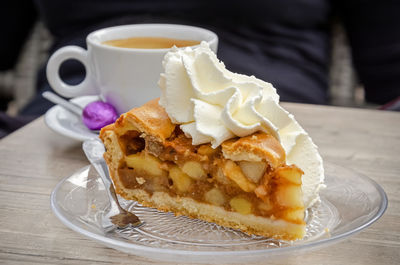 Apple pie with whipped cream on a terrace, as well as a cup of coffee with a purple easter egg