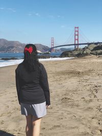 Rear view of woman with golden gate bridge over bay of water in background 