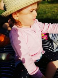 High angle view of cute baby girl wearing hat sitting in park during sunny day