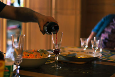 Cropped hand of man pouring wine in glass on table