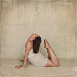 Side view of young woman sitting against wall