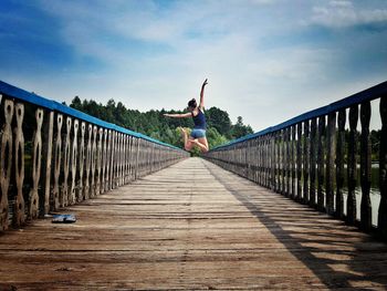 Woman jumping on bridge against sky
