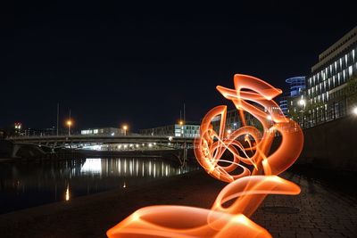 Light painting by river against sky in city at night