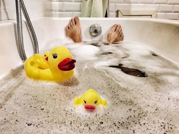 Low section of person with rubber ducks in bathtub at home