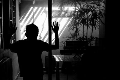 Rear view of silhouette boy with arms raised standing at home