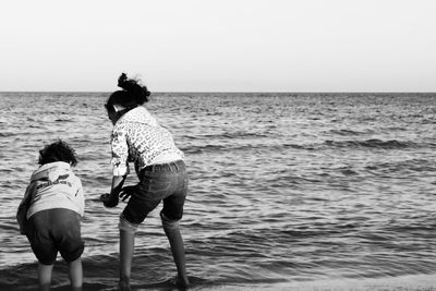 Rear view of women on sea shore against sky