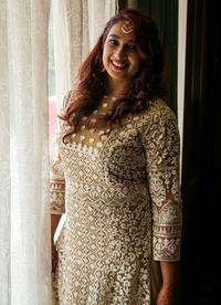Portrait of smiling young woman standing against curtain