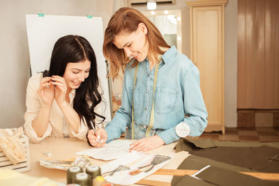 Women discuss model and project of future clothes, sketch on paper. fashionable sewing studio