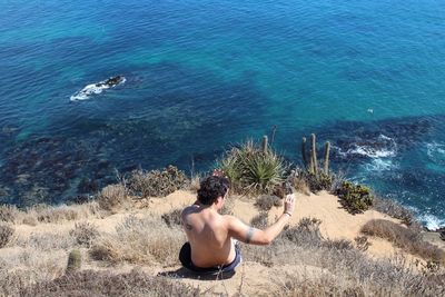 High angle view of shirtless man sitting on cliff against sea