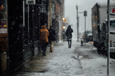 Rear view of people walking on street during snowfall