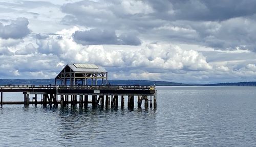 Stilt house on sea by building against sky