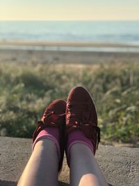 Low section of woman with feet up on railing against beach