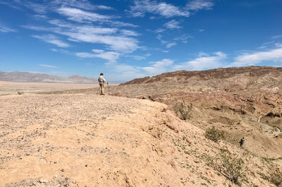Side view of senior man standing on sand at desert against blue sky