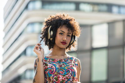 Fashionable young woman with curly hair listening music in city