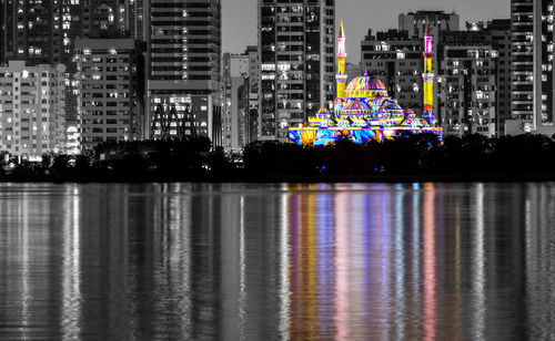 Illuminated mosque by lake in city at night