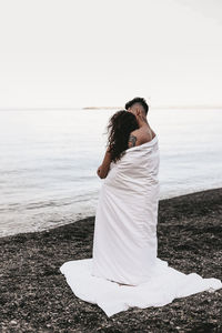 A couple in love spend the night at the sea, kissing and hugging on the beach covered with a blanket