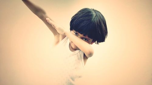 Portrait of boy doing dab dance against beige background