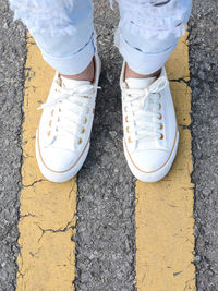Low section of person wearing canvas shoes while standing on road