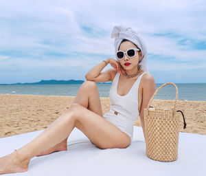 Young woman in sunglasses sitting at beach against sky