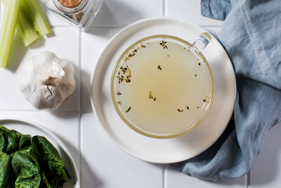 Healthy golden bone broth with spices in a mug on a saucer on a white background. 