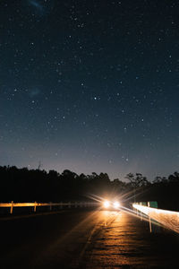 Road amidst illuminated street against sky at night