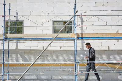 Side view of businessman with blueprint walking at incomplete building on sunny day