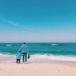 Rear view of men on beach against sky