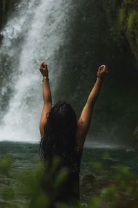 Rear view of woman with arms raised in forest