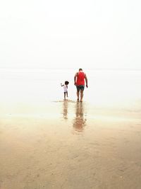 Rear view of father and son walking on beach