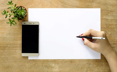 Cropped hand of woman writing in paper at table