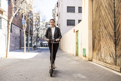 Portrait of woman riding push scooter on road