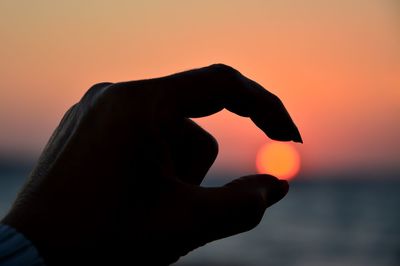 Close-up of silhouette hand against orange sunset sky