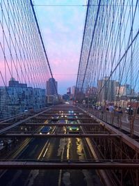 Suspension bridge in city against sky during sunset