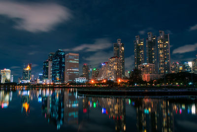 Illuminated buildings by river against sky at night