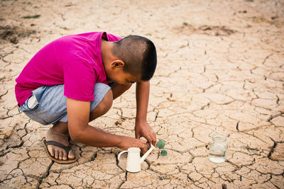 Boy planting plant on cracked field
