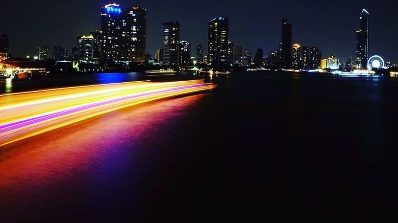 LIGHT TRAILS ON CITY STREET AGAINST ILLUMINATED BUILDINGS AT NIGHT