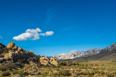 Small puff of white cloud in blue sky above rocky desert plain mountain meadow distant snowy peaks