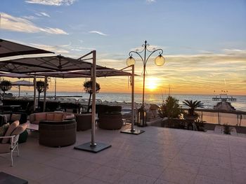 Chairs and tables by swimming pool against sky during sunset